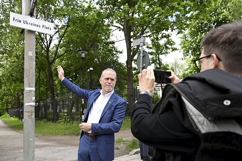 Stockholms dåvarande trafikborgarråd Daniel Helldén (MP) visar upp namnbyte utanför Rysslands ambassad 2022. Foto: TT